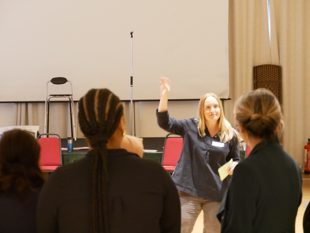 Photo of Sarah Marsay with hand in the air leading a session.